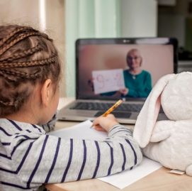Menina com tranças no cabelo assiste aulas no computador com coelho de pelúcia ao lado