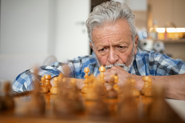 Homem parado em frente a um tabuleiro de xadrez analisando uma jogada.