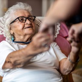Mulher idosa sentada segura a mão de uma pessoa em pé