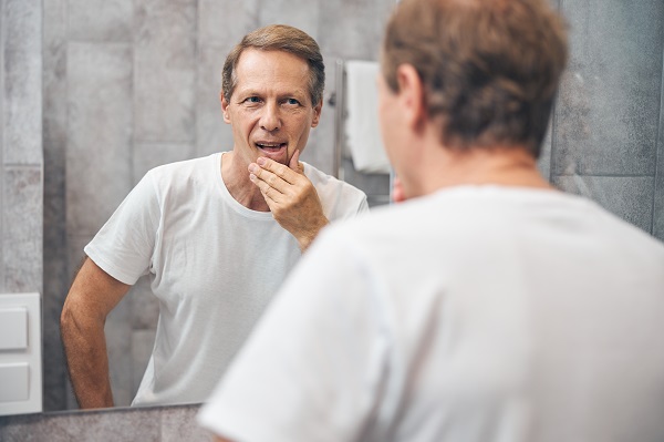 Homem segura o rosto enquanto olha no espelho 