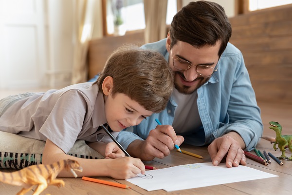 Homem sorri com o filho enquanto escreve em um papel 
