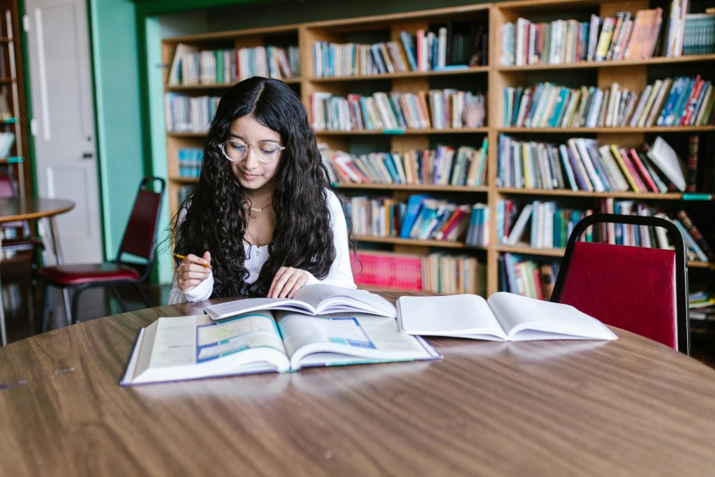Mulher jovem, de óculos, lendo em uma biblioteca