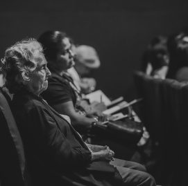 Foto em preto e branco com idosos sentados em uma plateia de teatro