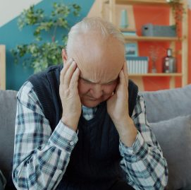 Idoso segurando a cabeça com as mãos, parecendo sentir uma forte dor